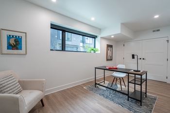 A living room with a desk and a chair and a window
